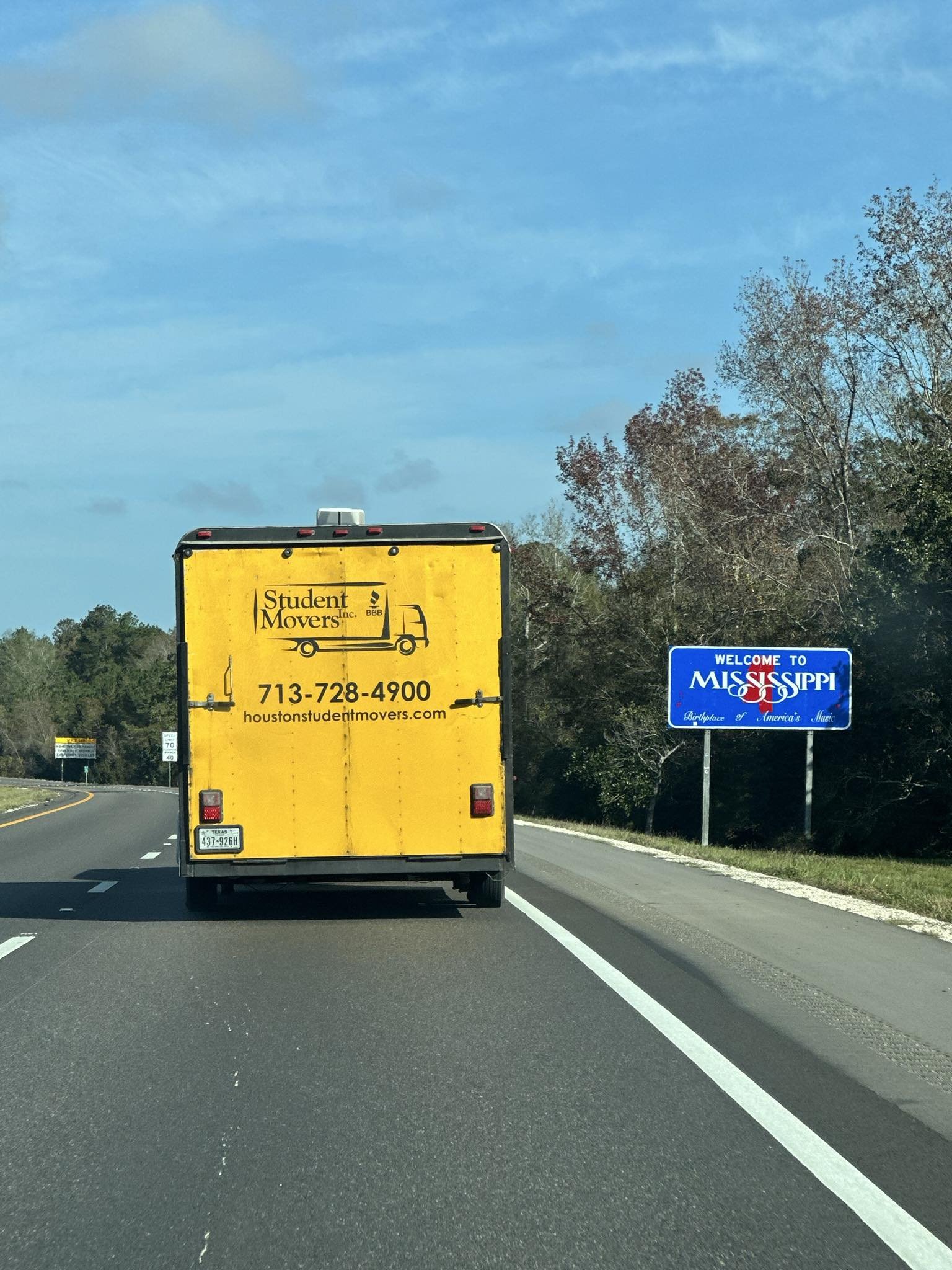 Student Movers yellow moving truck driving on a Houston highway toward a job.